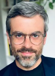 A man with grey hair and glasses is smiling.