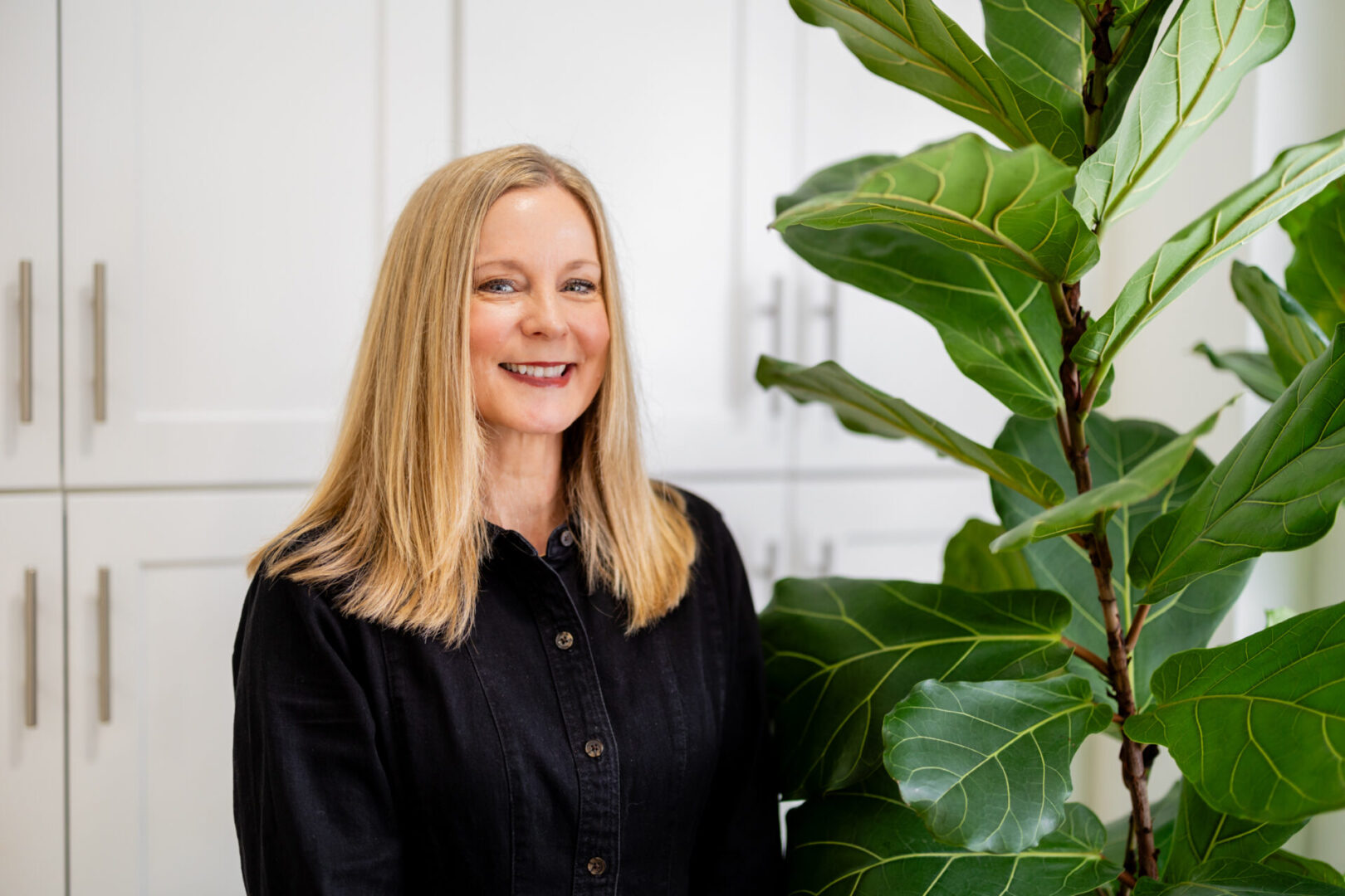 A woman standing next to a plant in her kitchen.